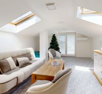 An attic room in a family house with a skylight, sofa, dresser, and television.