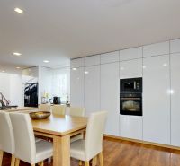 A kitchen in a family house with white furniture, a wooden decor floor, and a staircase.