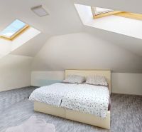Attic bedroom in a family house with a bed under skylights and a floor with a wooden decor.