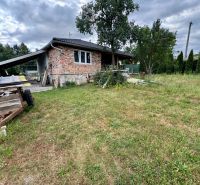 A family house in Ružiná with unplastered walls surrounded by a grassy garden and trees.