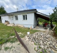 A family house in Ružiná with an unfinished facade and a shelter, surrounded by greenery.