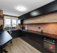A kitchen with a brick wall, black cabinets, and a wooden decor floor in a 2-room apartment.