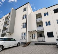 The exterior of an apartment building in Piešťany with a parking lot and white cars in front of a 1-bedroom apartment.