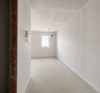 An empty interior of a one-room apartment with white walls and a concrete floor.