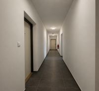 A corridor with white walls and tiles leading to the door in a studio apartment.