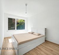 A bedroom with wood-patterned flooring, a large window, and a white bed in a two-room apartment.