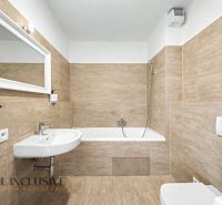 A bathroom in a 2-room apartment with a bathtub, a mirror, and beige tiles.