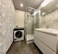 A bathroom in a 3-room apartment with a washing machine, shower, and sink.