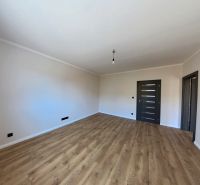 An empty room with a wooden floor and dark doors in a 3-room apartment.