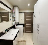 A bathroom in a 3-room apartment with a sink, mirror, cabinets, and a washing machine.