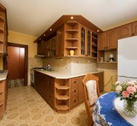The kitchen of a 4-room apartment with a wooden decor, flowers on the table, cabinets, and appliances.