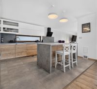 A kitchen in a family house with an island, bar stools, and a floor with a wooden decor.