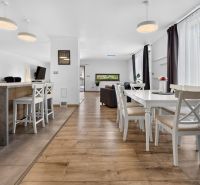Dining room in a family house with a wooden decor floor, white furniture, and windows.