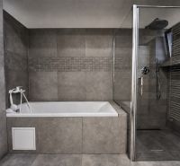 A bathroom in a family house with a bathtub, a shower corner, and gray tiles.