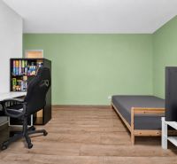 A room in a family house with a desk, chair, bed, and a floor with a wooden decor.