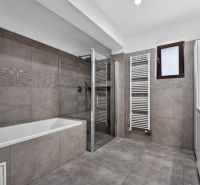 A bathroom in a family house with a bathtub, shower corner, and towel radiator.