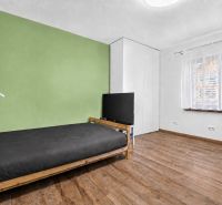 A room in a family house with a bed, TV, green wall, and floor with a wooden decor.