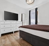 Bedroom in a family house with a white dresser, television, and a bed on the floor with a wooden decor.