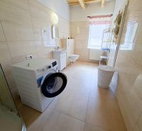 A bathroom in a family house with a washing machine, shower, and a window with a pink curtain.