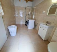 Bathroom in a family house with a washing machine and a shower, light tiles.