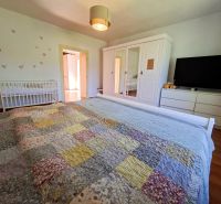 A bedroom with a wood-patterned floor in a family house, with a large bed and a baby crib.