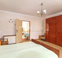 A bedroom in a family house with retro furniture and patterned wallpaper on the wall.