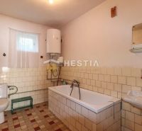A bathroom with a tiled bathtub and a boiler in a family house.