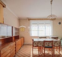 A dining room in a family house with retro furniture and a carpet, dominated by a bright window.