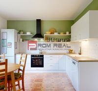 A kitchen in a family house with a light-colored kitchen unit, a dining table, and a green wall.