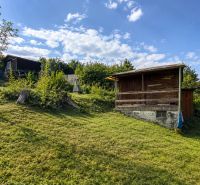A wooden cottage in Žilina surrounded by green lawns and trees on a sunny day.