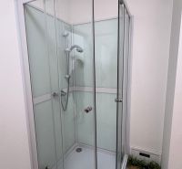 Shower enclosure in commercial premises with tiles and glass doors.
