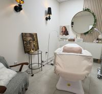Beauty salon with a lounger, wall decorations, and a round mirror.