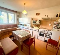 A kitchen with a dining area, an older stove, and a wooden-patterned floor in a family house.