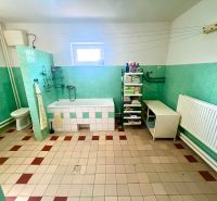 Bathroom in a family house with a bathtub, toilet, shelves, and a window.
