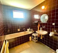 A bathroom in a family house with dark tiles, a bathtub, and a window on the wall.