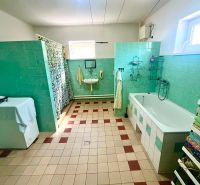 A bathroom in a family house with green tiles, a bathtub, and a washing machine.