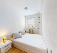 Bedroom in a 2-room apartment with a white bed, nightstand, and wooden decor flooring.