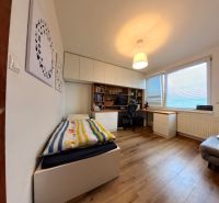 A room in a 4-room apartment with a wooden decor floor, a table, and a bed.