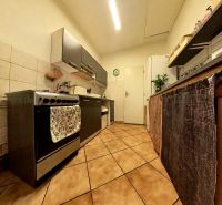 A narrow kitchen in a family house with ceramic tiles and a stainless steel stove.