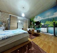 A bedroom in a family house with a bed, wall wallpaper, and a floor with a wooden decor.