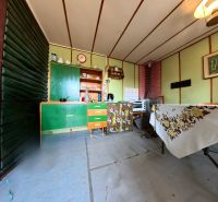 Interior of a cabin with older furniture, a hotplate on the counter, and floral textile decor.