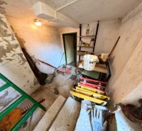 A shed with garden tools and a lawnmower, stored on stairs and shelves.