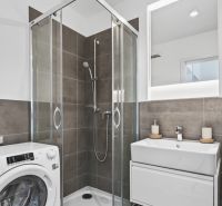 A bathroom in a studio apartment with a shower, a sink, and a washing machine.