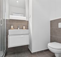 A bathroom in a studio apartment with a sink, shower, and toilet, tiled with tiles.