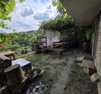 A cottage in Banská Bystrica with rustic seating and vine, surrounded by nature.