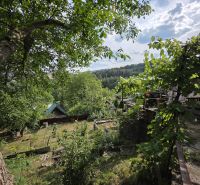 A cottage in Banská Bystrica surrounded by greenery and forest, with a view of the surrounding landscape.