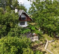 A cottage in Banská Bystrica surrounded by dense forest and green vegetation.