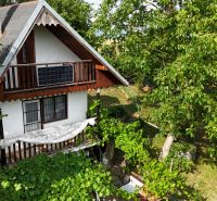 A cottage in Banská Bystrica surrounded by greenery with a wooden balcony and a photovoltaic panel.