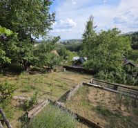 A garden by the cottage in Banská Bystrica surrounded by trees and hills on the horizon.
