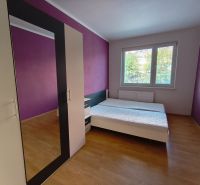 A bedroom in a three-room apartment with a wooden decor floor and purple walls.